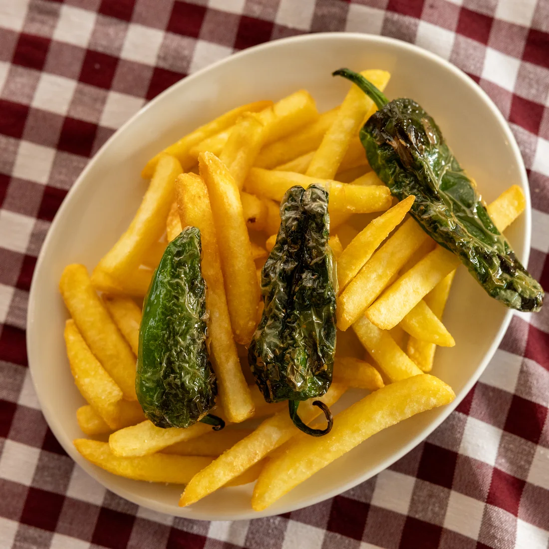 Patatas fritas caseras con pimientos de padrón fritos sobre mantel de cuadros